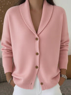 Hélène shawl-collar cardigan in pink, closed with four wooden buttons and worn with white trousers.