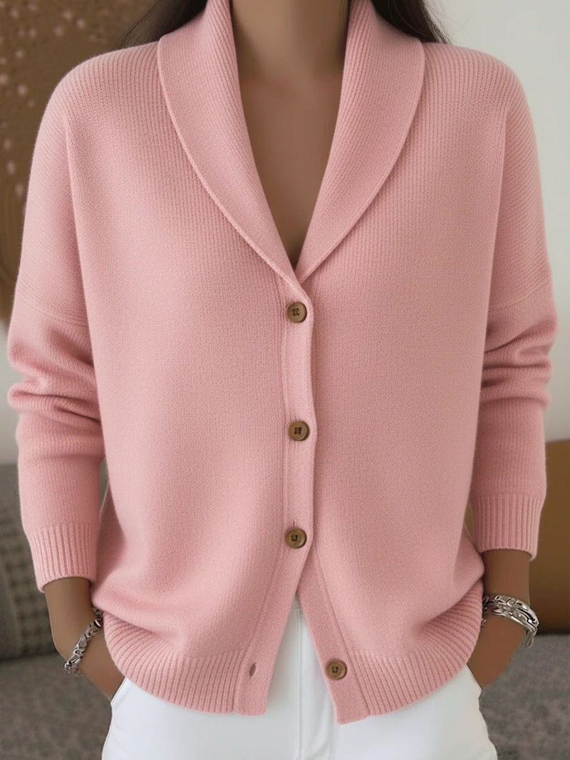 Hélène shawl-collar cardigan in pink, closed with four wooden buttons and worn with white trousers.
