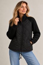 Lena quilted jacket – black, zipped up with hands in the front pockets