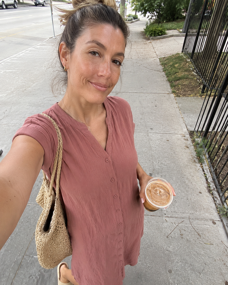 Woman wearing the Odette shirt dress in rose, outdoors with an iced coffee and a straw bag